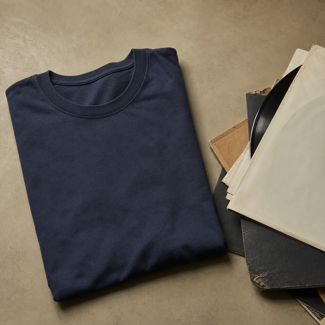 Folded muted-navy t-shirt beside a small stack of mismatched vinyl records